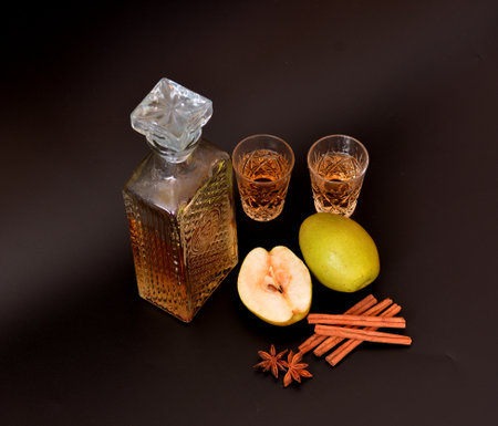Pear liqueur with cinnamon and anise, homemade alcohol in a crystal bowl on a black background, next to ripe fruits and spices. Close-up.の写真素材