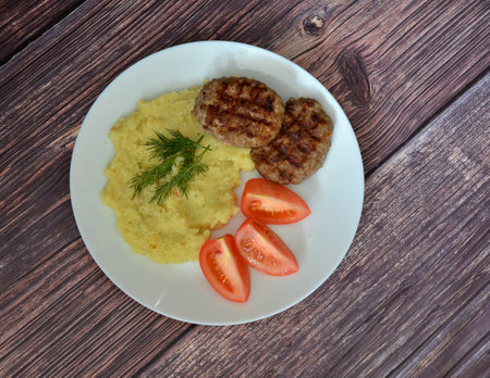 Two fried cutlets, mashed potatoes with a sprig of dill and ripe tomato slices on a wooden table. Top view, flat lay.の写真素材