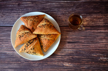 Samsa, several pieces, decorated with sesame seeds on a dark wooden table. Top view, flat lay.
