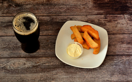 A tall and wide glass of dark beer and a plate of wheat croutons with garlic sauce on a dark wooden...