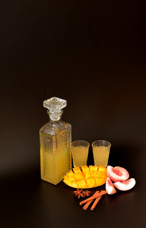 Mango-peach liqueur with cinnamon and anise in a crystal decanter and two glasses on a black background. Close-up.の写真素材