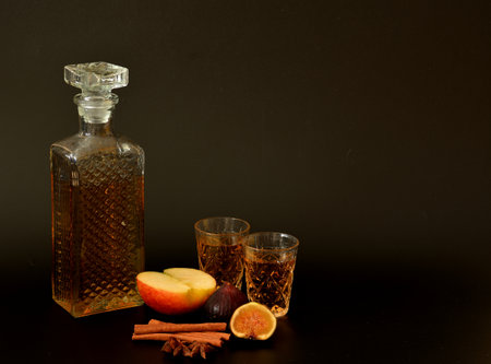 Apple-fig liqueur with cinnamon and anise on a black background, homemade in a decanter and two glasses next to ripe fruits. Close-up.の写真素材