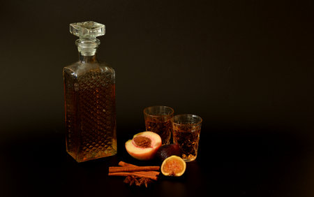 Fig-plum liqueur with spices on a black background, a crystal decanter and two glasses of alcohol, next to ripe fruit. Close-up.の写真素材