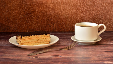 A piece of Italian dessert Tiramisu, a cup of hot black coffee and a table fork on a wooden table....