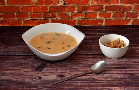 Cheese cream soup with mushrooms in a deep plate, a cup with croutons and a spoon on a wooden table. Close-up.の写真素材