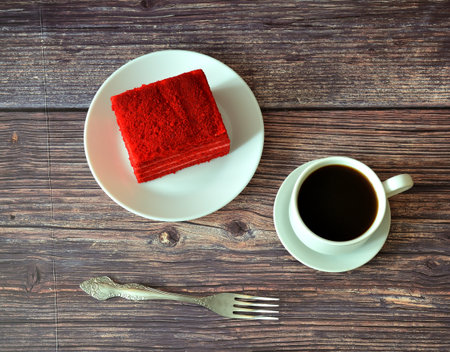 A piece of red velvet layer cake on a round plate, a table fork and a cup of black coffee on a wooden table. Top view, flat lay.の写真素材