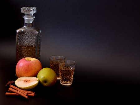 Apple liqueur in a crystal decanter and two glasses on a black background, next to pieces of ripe fruit and cinnamon with anise. Close-up.の写真素材