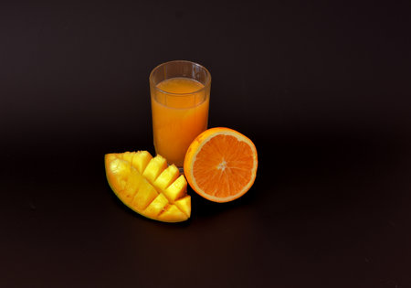 Mango juice with orange in a tall glass on a black background, next to pieces of ripe fruit. Close-up.の写真素材