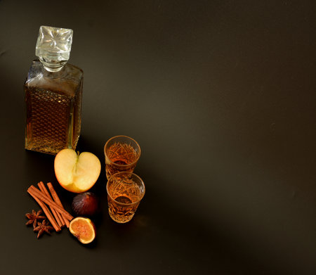Fig-apple liqueur with cinnamon and anise on a black background, strong alcohol in crystal vessels, ripe fruits and spices nearby. Close-up.の写真素材