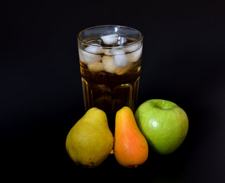 Apple and pear juice with ice on a black background, a tall faceted glass of juice and ripe fruits nearby. Close-up.の写真素材