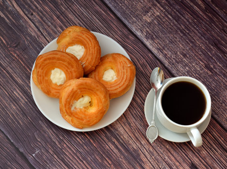 A cup of black coffee on a saucer with a spoon and a plate with four custard cakes with protein...