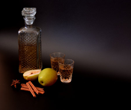 Pear-apple liqueur with cinnamon and anise in a crystal decanter and two glasses on a black background. Close-up.の写真素材