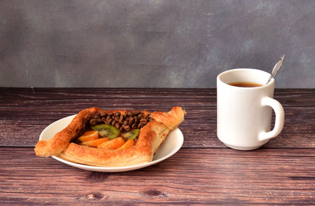 Puff pastry bun with mandarin, kiwi and coffee beans with a cup of black tea on a wooden table. Close-up.の写真素材