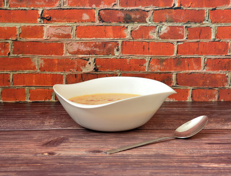 Delicious and nutritious cheese cream soup with smoked meat in a deep ceramic plate on a wooden table, a tablespoon nearby. Close-up.の写真素材