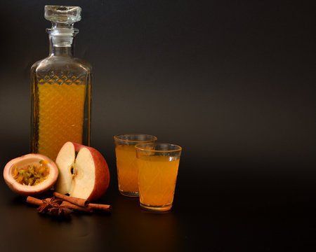 Apple-passion fruit liqueur with cinnamon and anise in crystal glass on black background, spices and pieces of ripe fruit nearby. Close-up.の写真素材