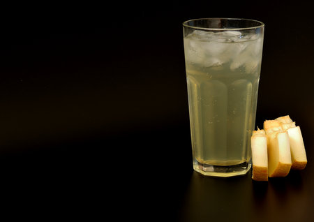 A tall, faceted glass of melon juice with ice on a black background, with pieces of ripe fruit nearby. Close-up.の写真素材