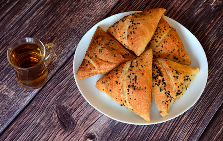 A plate with several fresh oriental meat buns samsa and a glass cup with tea on a wooden table. Top view, flat lay.の写真素材