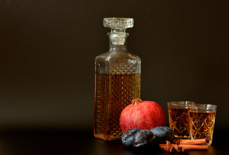 Plum-pomegranate liqueur with spices on a black background, homemade strong alcohol with cinnamon and anise in a crystal bowl. Close-up.の写真素材