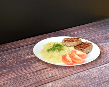 Two fried cutlets, tomato and mashed potatoes with green onions on a wooden table. Close-up.の写真素材