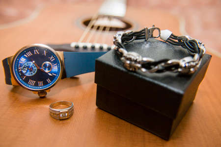 Wrist watch, gold ring, bracelet and acoustic guitar in the background