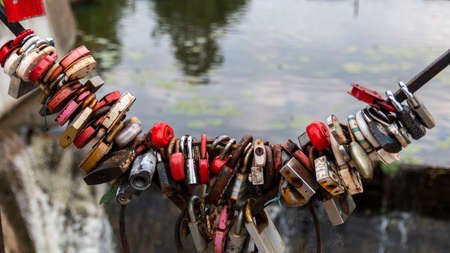Multicolored padlocks hanging on a bridge on a lake backgroundのeditorial素材