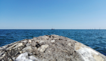Landscape of grey stone  with white small shells at the port seaside the blue wave ocean sea with clearly blue sky, the small boat transports in the seaのeditorial素材
