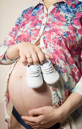 Small shoes for the unborn baby in the belly of pregnant womanの写真素材