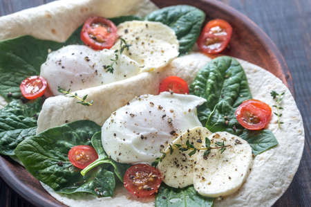 Tortilla sandwiches with poached eggs, mozzarella, spinach and cherry tomatoesの写真素材