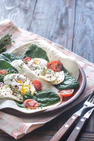 Tortilla sandwiches with poached eggs, mozzarella, spinach and cherry tomatoesの写真素材