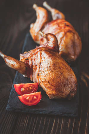 Two baked quails wrapped in bacon on the black stone boardの写真素材