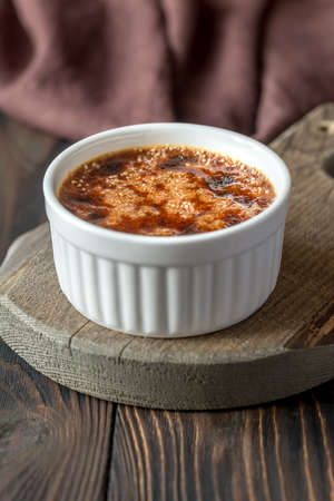 Creme brulee in the white pot on the wooden board