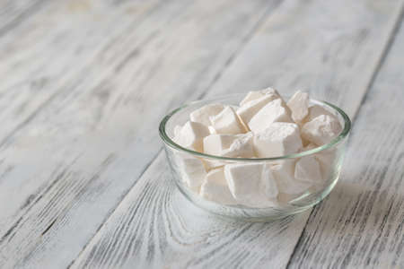 Glass bowl of white lump sugar on the wooden background