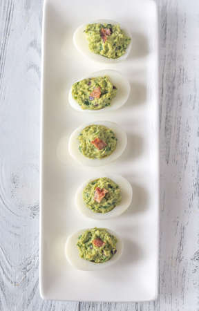 Guacamole and bacon deviled eggs on the white plate