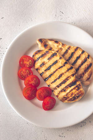 Grilled chicken breast with cherry tomatoes on the white plateの写真素材
