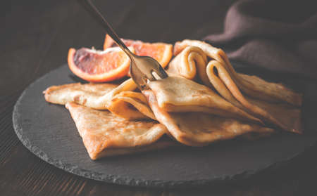 Crepes Suzette with slices of blood orange on the black stone board