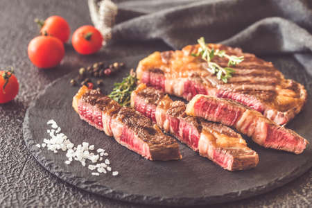 Grilled beef steak garnished with cherry tomatoes and thyme on the black stone boardの写真素材
