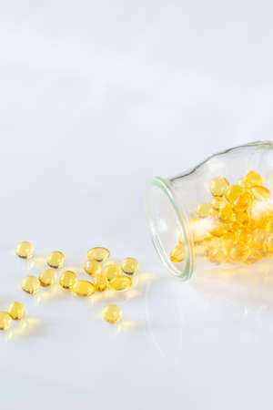 Omega-3 fish oil capsules pouring out from the glass jar on the white background