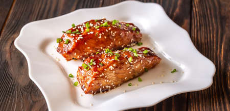 Two pieces of teriyaki salmon garnished with sesame seeds and spring onion