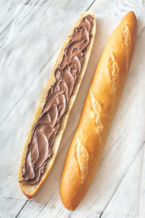 Half of baguette with chocolate cream on the wooden table