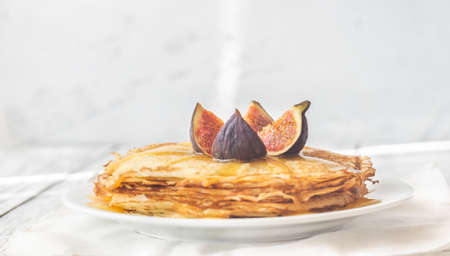 Stack of homemade crepes with fresh fig and sweet topping on the white plateの写真素材