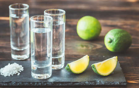 Glasses of tequila with lime wedges on the stone boardの写真素材