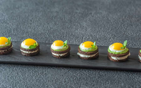 Canape with cream cheese, guacamole and fried quail eggs on the plate