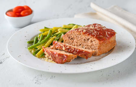 Meatloaf topped with tomato sauce with green beansの写真素材