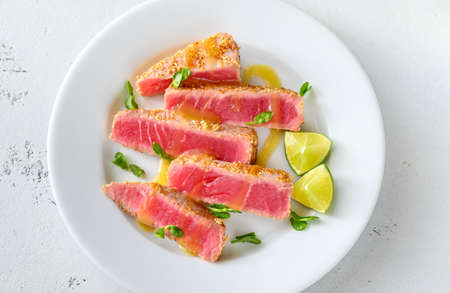 Tuna steak with sesame seeds with herbs and lime wedgesの写真素材