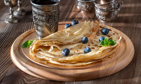 Crepes with fresh blueberries and berry syrup on wooden board