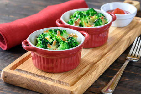 Two pots with baked broccoli and cheese on wooden boardの写真素材