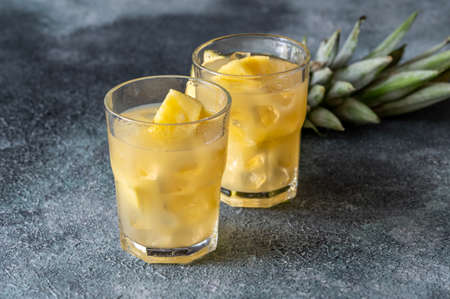 Two glasses of pineapple juice with pieces of fresh fruit
