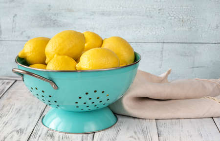 Fresh lemons in blue colander. Wooden backgroundの写真素材