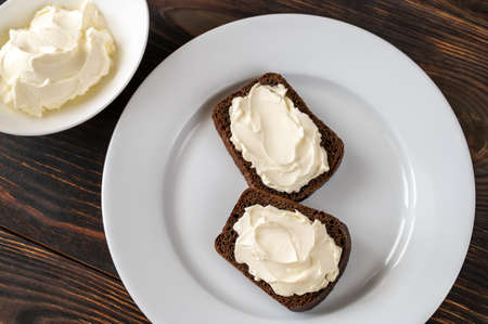 Slices of rye bread with cream cheese on white plateの写真素材