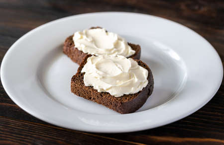 Slices of rye bread with cream cheese on white plate